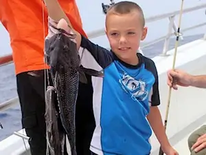 Child fishing with their parents holding up a black sea bass and triggerfish on an offshore bottom fishing charter on the Outer Banks.